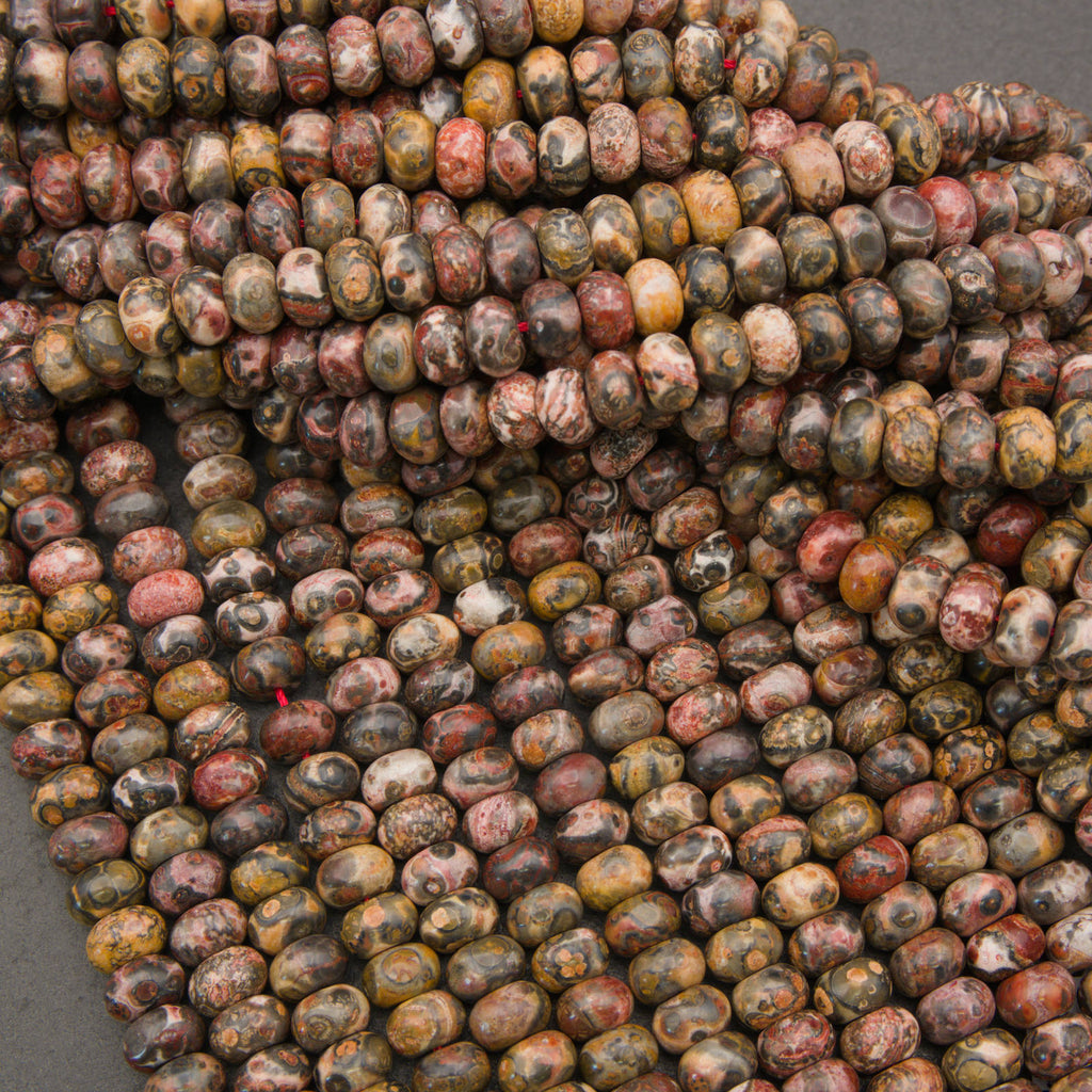 A close-up pile of polished oval beads with a mottled, marbled pattern in earthy tones of brown, beige, red, and gray.