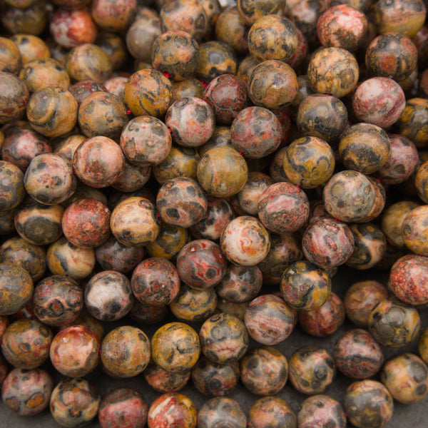 A close-up pile of round gemstone beads with a mottled marbled pattern in earthy tones of brown, yellow, red, and gray.