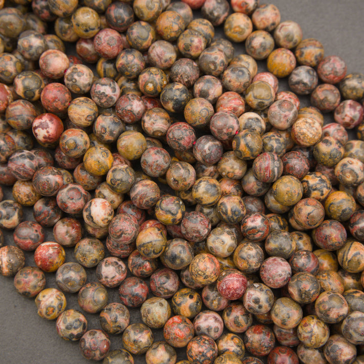 A pile of round, polished gemstone beads in earthy, mottled colors including brown, red, yellow, and black, arranged on a dark gray background.