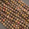A pile of round, polished gemstone beads in earthy, mottled colors including brown, red, yellow, and black, arranged on a dark gray background.