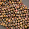 A pile of round gemstone beads in earthy, mottled colors including brown, yellow, red, and gray, arranged on a dark gray surface.