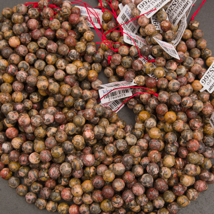 A pile of small round gemstone beads in earthy marbled colors, many tied with red string and attached to white barcode price tags, photographed on a gray surface.