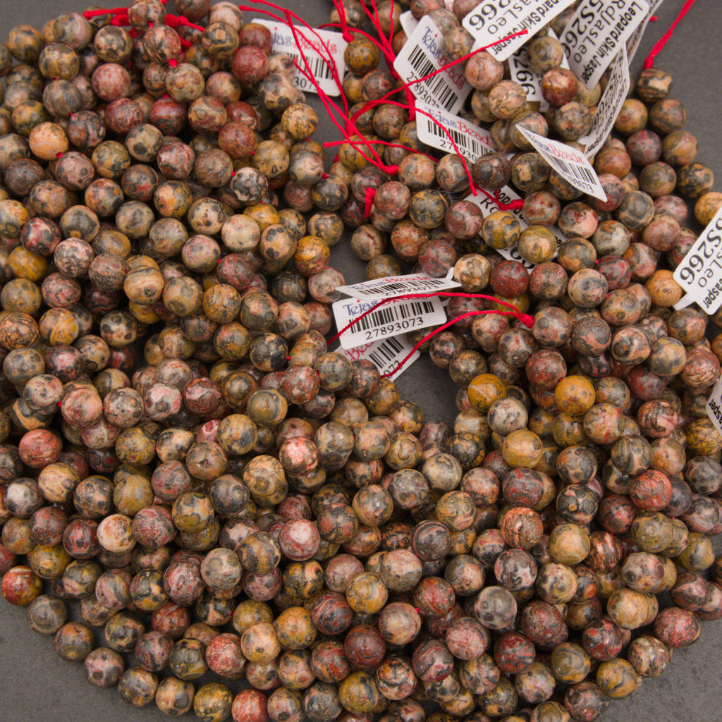 A pile of small round gemstone beads in earthy marbled colors, many tied with red string and attached to white barcode price tags, photographed on a gray surface.