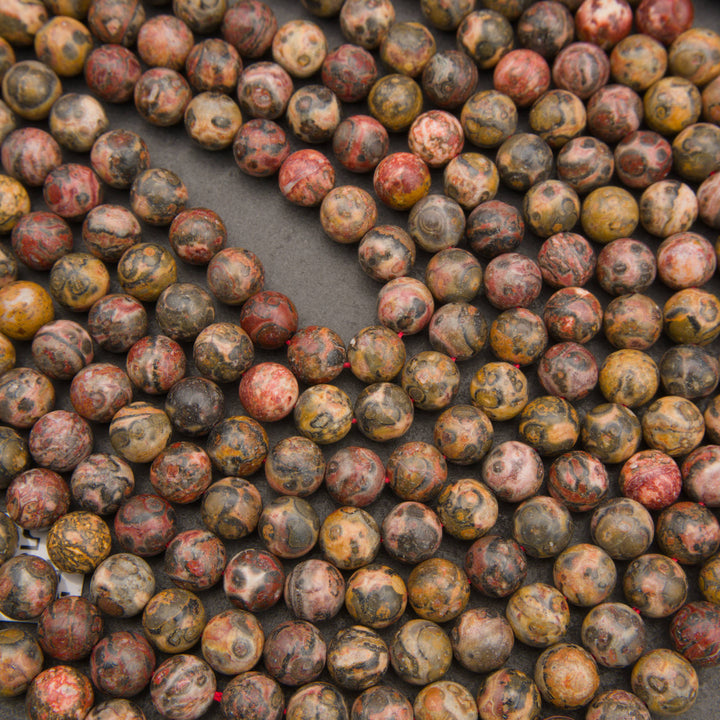 A close-up arrangement of many round stone beads in earthy mottled colors, including brown, beige, red, gray, and black, filling the frame.