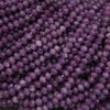 A close-up pile of faceted purple beads, likely amethyst, showing a consistent round shape and polished crystal facets.