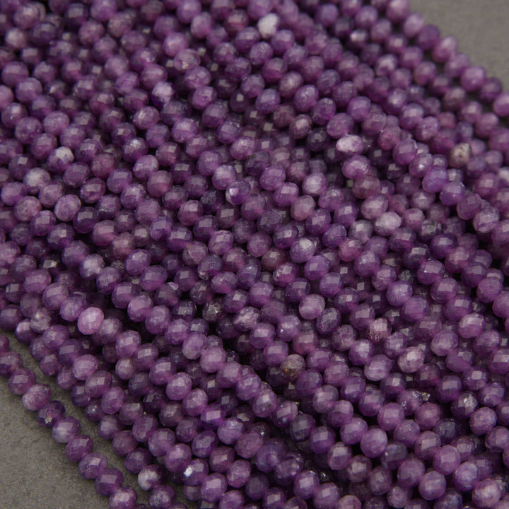 Multiple strands of faceted purple beads, likely amethyst, arranged diagonally on a neutral gray surface.