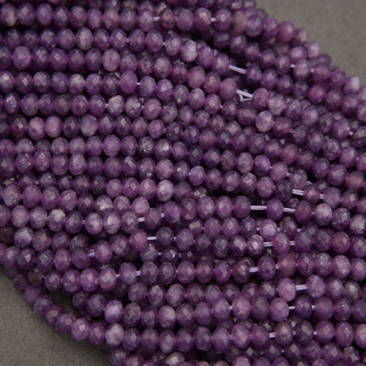 Multiple strands of faceted purple beads, likely amethyst, arranged closely together on a neutral gray surface.