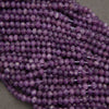 Multiple strands of faceted purple beads, likely amethyst, arranged closely together on a neutral gray surface.