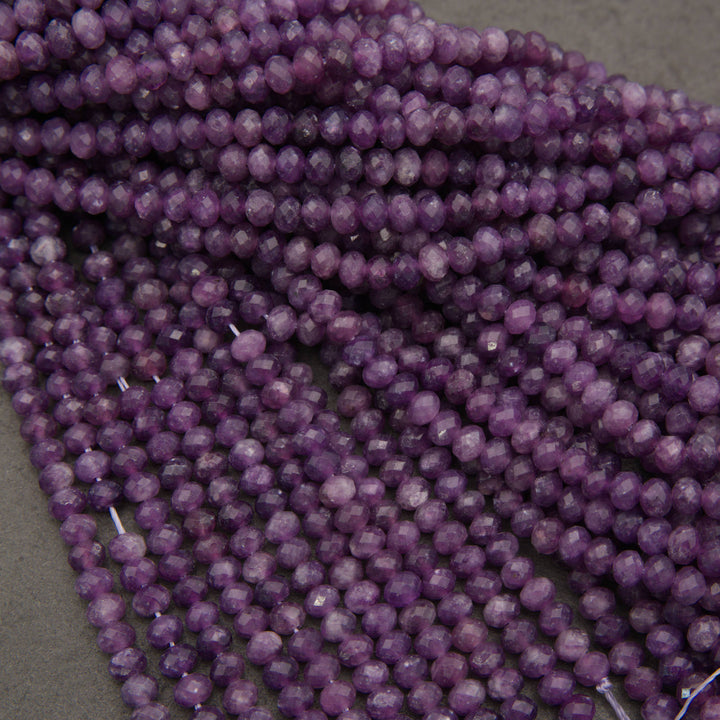 Multiple strands of faceted purple beads, likely amethyst, arranged in overlapping rows on a neutral gray surface.