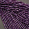 Multiple strands of faceted purple beads, likely amethyst, arranged in overlapping rows on a neutral gray surface.