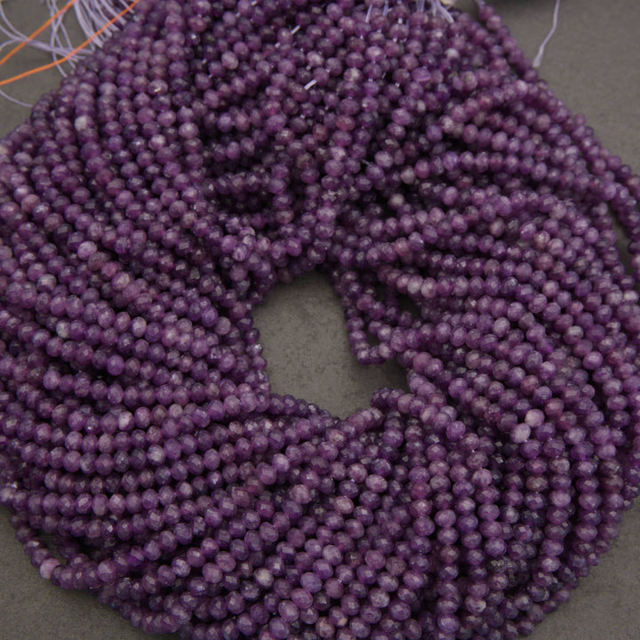 Multiple strands of faceted purple beads coiled together on a neutral gray surface.