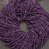Multiple strands of faceted purple beads coiled together on a neutral gray surface.
