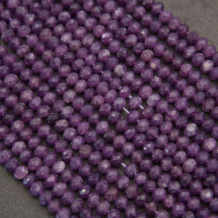 Purple faceted gemstone beads strung on a cord, arranged in parallel rows on a neutral gray background.
