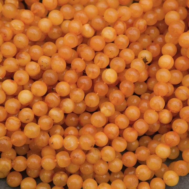 A close-up pile of small, round, translucent orange beads with a glossy finish.