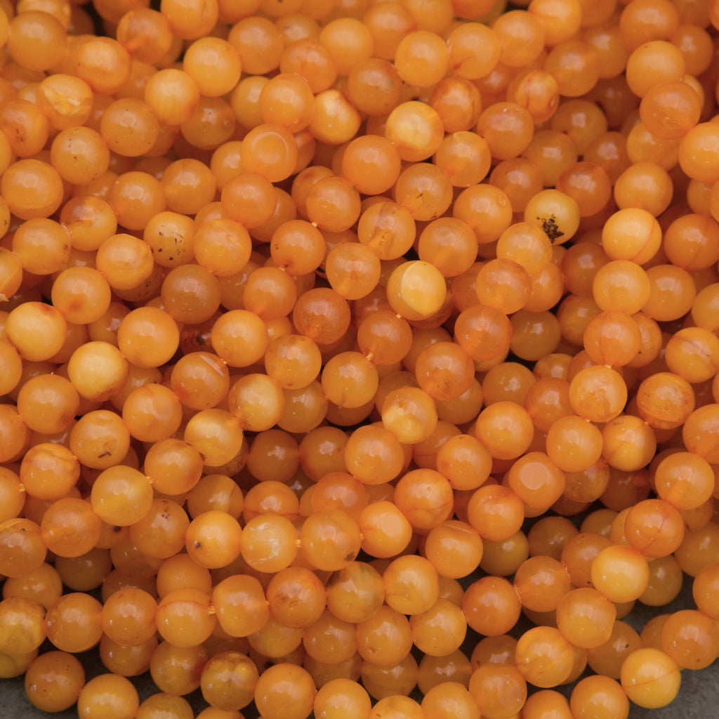 A close-up pile of small, round, translucent orange beads with a glossy finish.