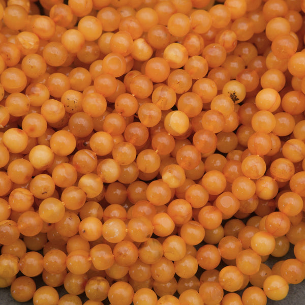 A close-up pile of small, round, translucent orange beads with a glossy finish.