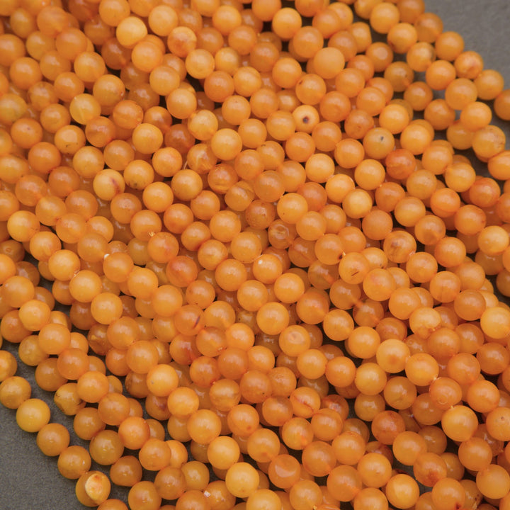 A close-up pile of small, round, translucent orange-yellow beads on a dark gray surface.