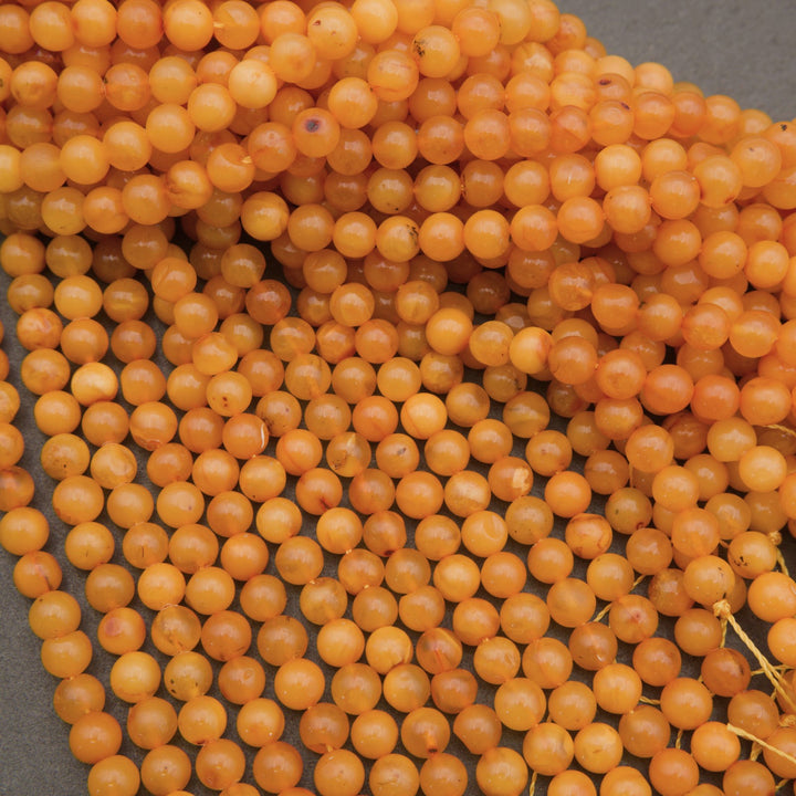 A pile of small, round, translucent orange beads strung on cords, filling the frame against a dark gray background.