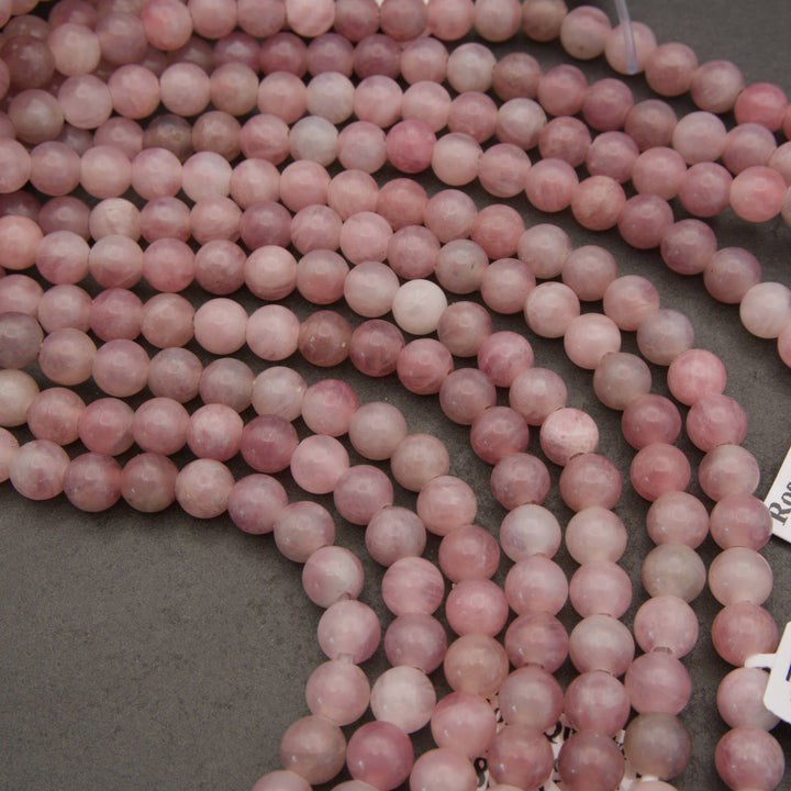 Curved strands of round pink rose quartz beads on a dark gray background.