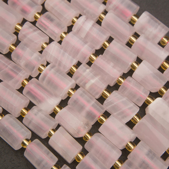 A close-up of a beaded strand featuring translucent pale pink rose quartz cylindrical beads separated by small metallic gold spacer beads, laid flat on a dark gray background.