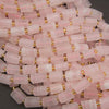 A pile of cylindrical pink stone beads with small gold spacer rings, shown close up on a dark background.