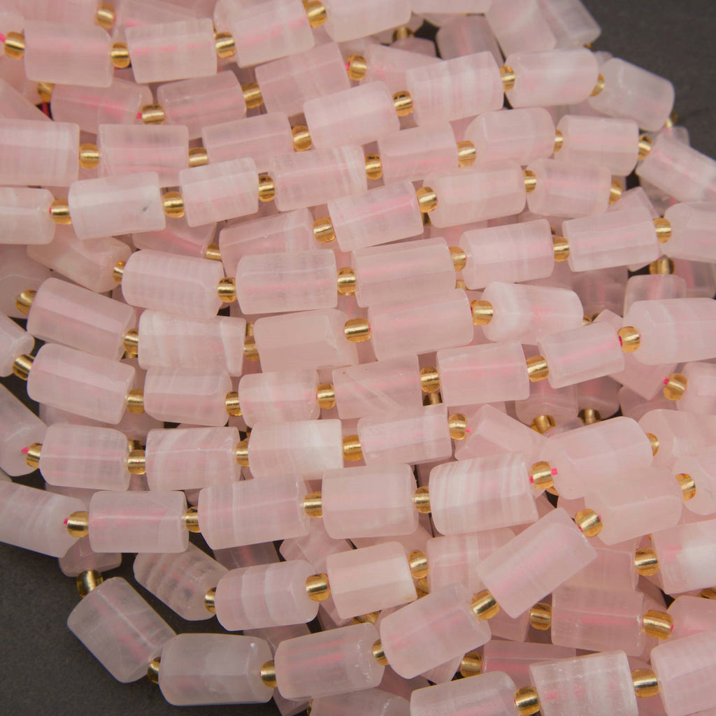 A pile of cylindrical pink stone beads with small gold spacer rings, shown close up on a dark background.