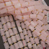 A pile of cylindrical pink stone beads with small gold spacer rings, shown close up on a dark background.