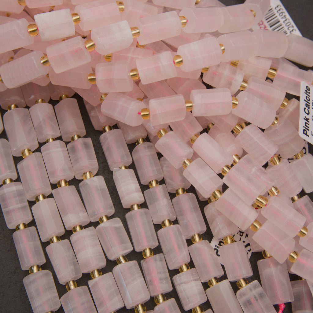 A pile of cylindrical pink stone beads with small gold spacer rings, shown close up on a dark background.