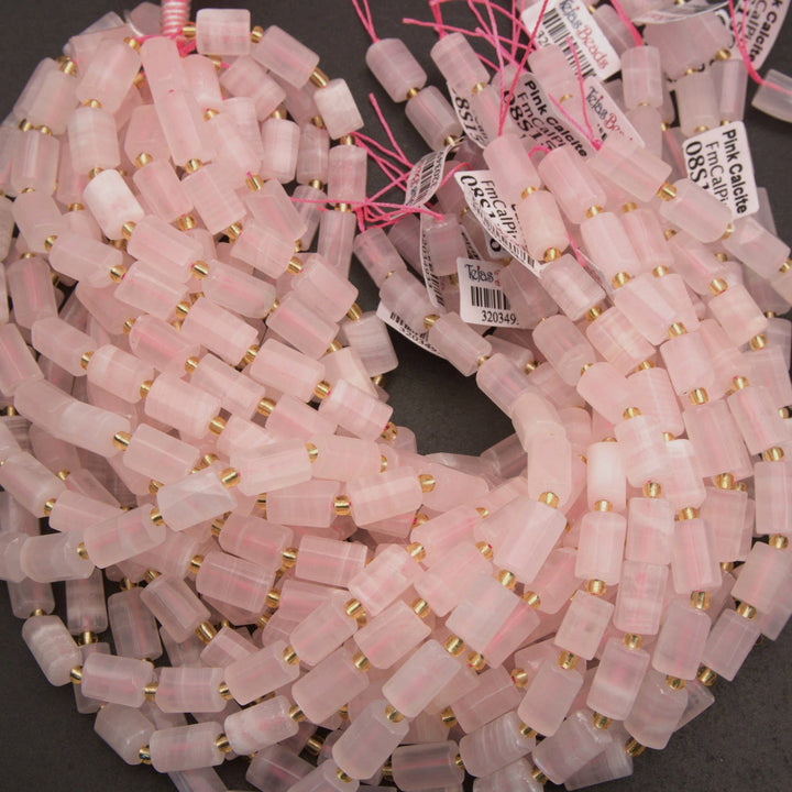 A large coil of pink translucent stone beads with small gold spacer rings, photographed on a dark surface. Several white product tags are visible among the beads.