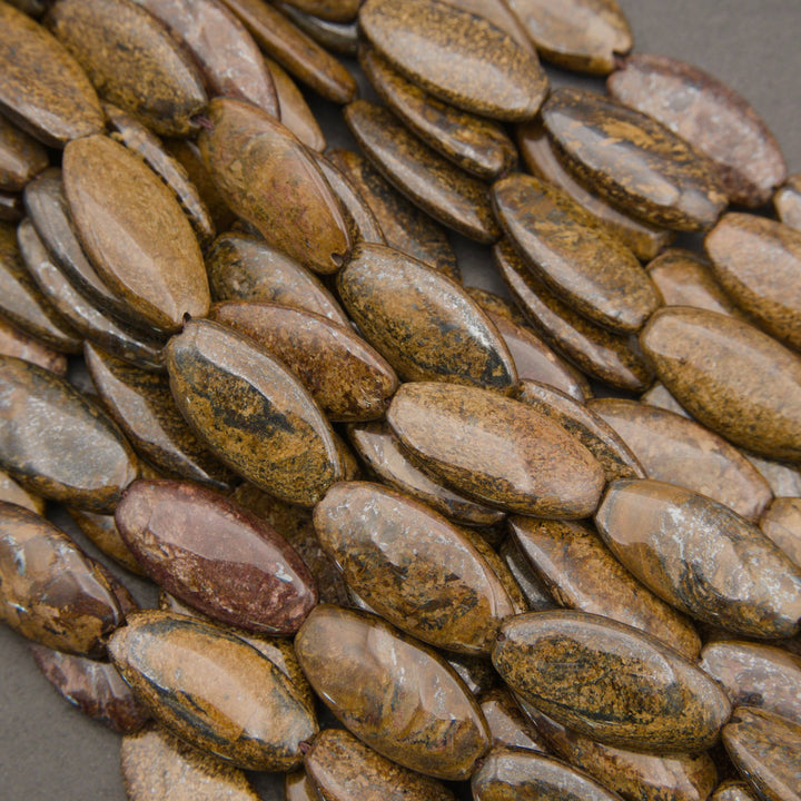 A close-up pile of polished oval gemstone beads in earthy brown, tan, and gray tones with natural marbled patterns.