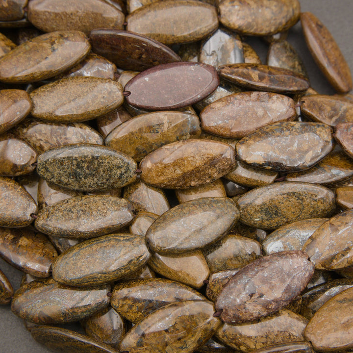 A close-up pile of polished oval gemstones in earthy brown, tan, and gray tones.