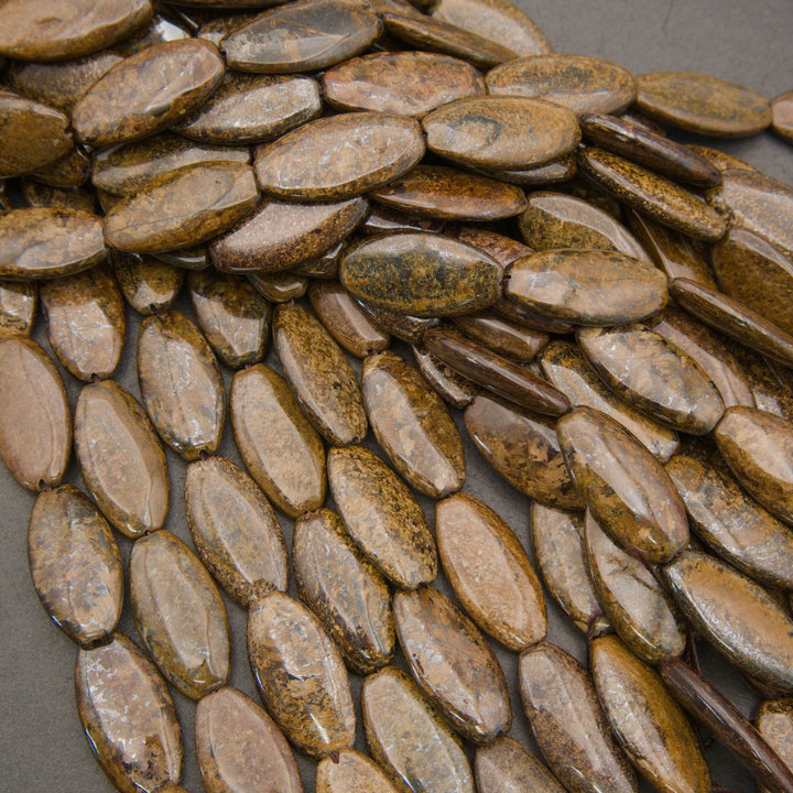 A pile of polished oval stone beads in earthy brown, tan, and olive tones on a dark gray background.
