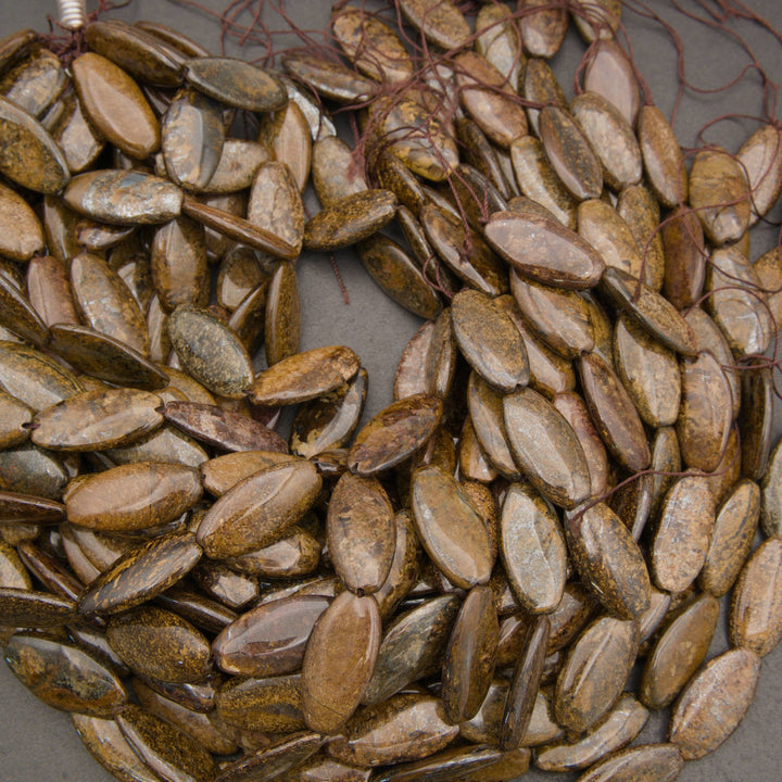 A pile of small, polished, olive-brown seed or nut-shaped beads with natural striated patterns, strung on thin brown cords.