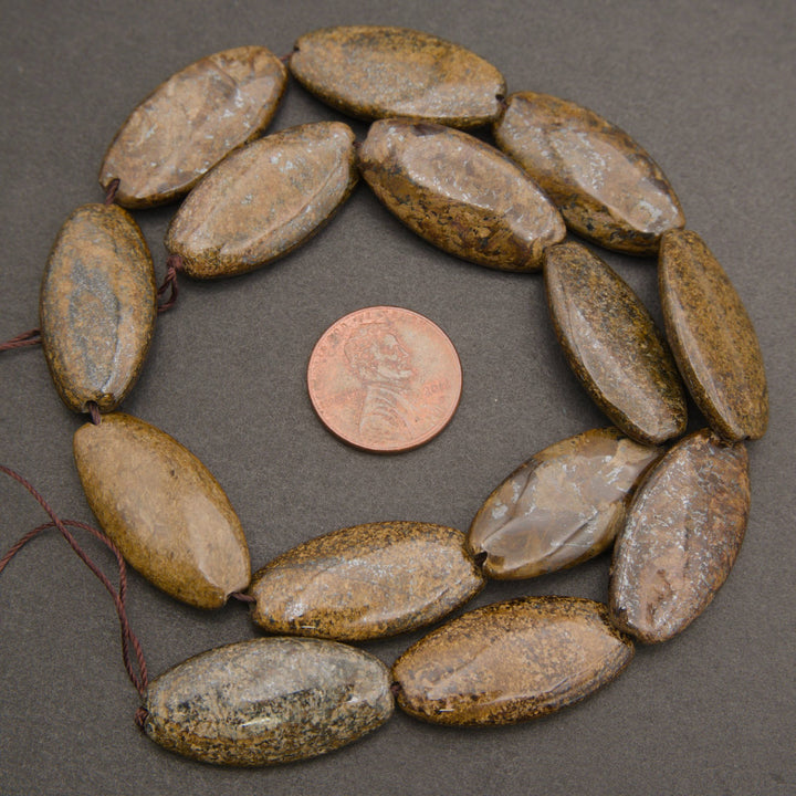 A strand of polished brown and tan stone beads arranged in a circle on a dark gray background, with a copper coin placed in the center for scale.