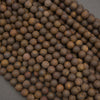 A close-up pile of small round brown beads with natural wood-like texture and subtle tan variation, photographed on a dark gray surface.