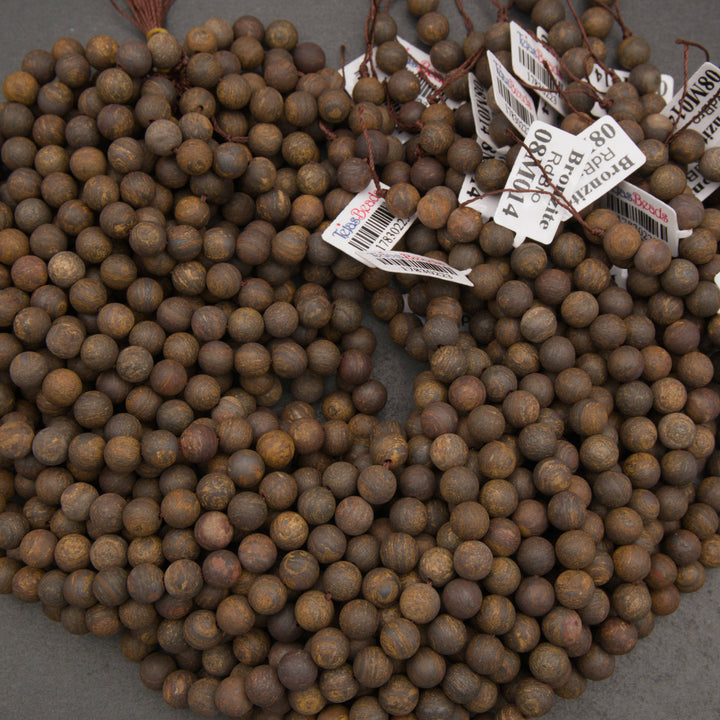 A large pile of small round wooden beads in a medium brown color, with several white inventory tags attached near the top on a gray surface.