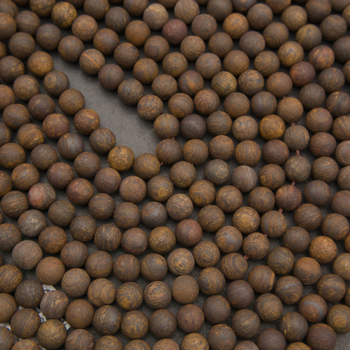 A close-up arrangement of many small round brown beads or wooden discs with visible wood grain, filling the frame on a dark surface.