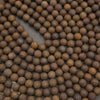 A close-up arrangement of many small round brown beads or wooden discs with visible wood grain, filling the frame on a dark surface.