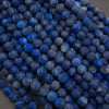 A pile of small round blue lapis lazuli stone beads with natural white and yellow veining, photographed close-up on a neutral gray surface.