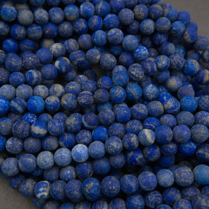 A close-up pile of round lapis lazuli stone beads in deep blue with white marbling, filling the frame.