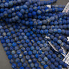 A pile of round blue lapis lazuli stone beads with natural white and light blue veining, shown on a neutral gray background with some white inventory tags visible.