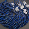 Multiple strands of round blue lapis lazuli stone beads with white price tags attached, arranged on a dark gray surface.