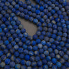 A close-up of many round blue beads with natural white and gray marbling, arranged in a loose heart shape on a neutral surface.