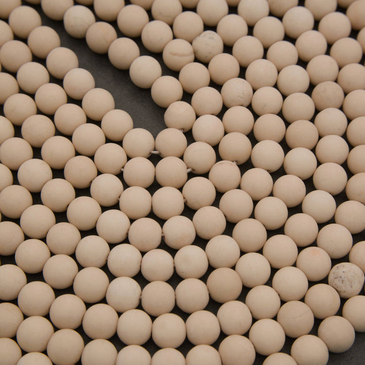 A close-up view of many small round beige ceramic beads or balls arranged closely together on a dark surface.