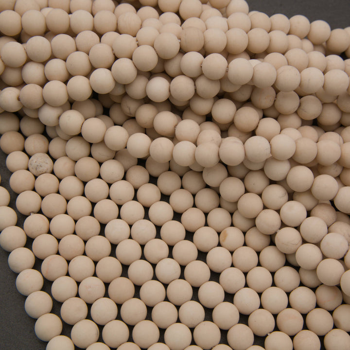 A close-up pile of small, round, off-white ceramic beads or balls filling the frame against a dark gray background.