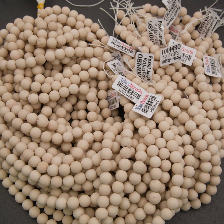 A large pile of round, light beige wooden beads with white price tags attached, photographed on a dark gray surface.