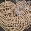 A large pile of round, light beige wooden beads with white price tags attached, photographed on a dark gray surface.