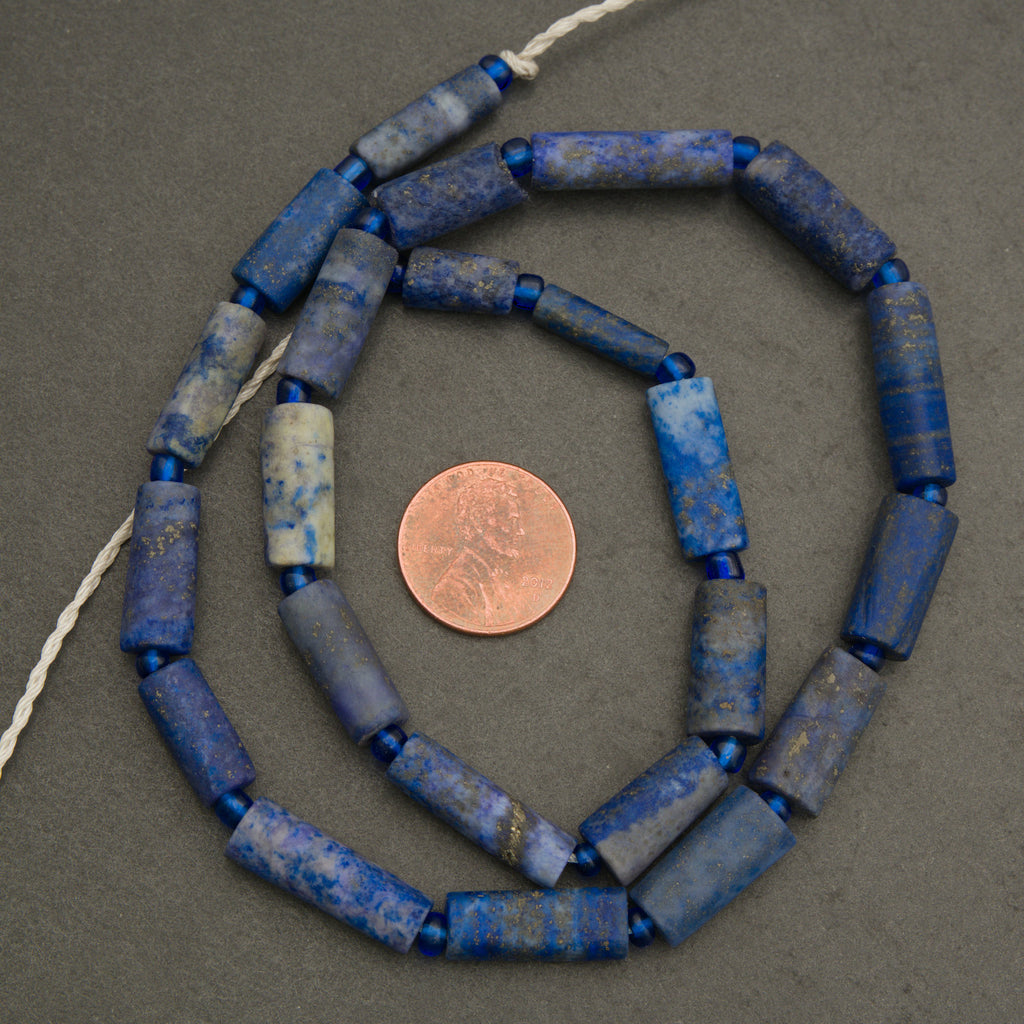 String of blue beads with a penny for scale on a gray background
