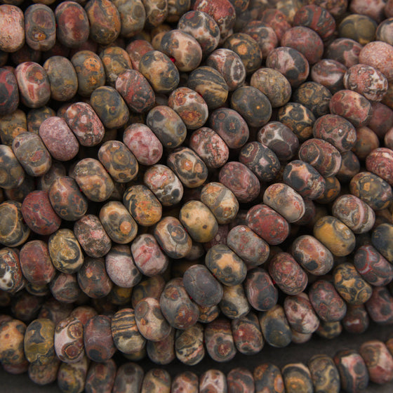 A close-up pile of polished oval beads made from mottled stone, showing varied earthy colors and marbled patterns.