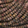 A close-up pile of polished oval beads made from mottled stone, showing varied earthy colors and marbled patterns.